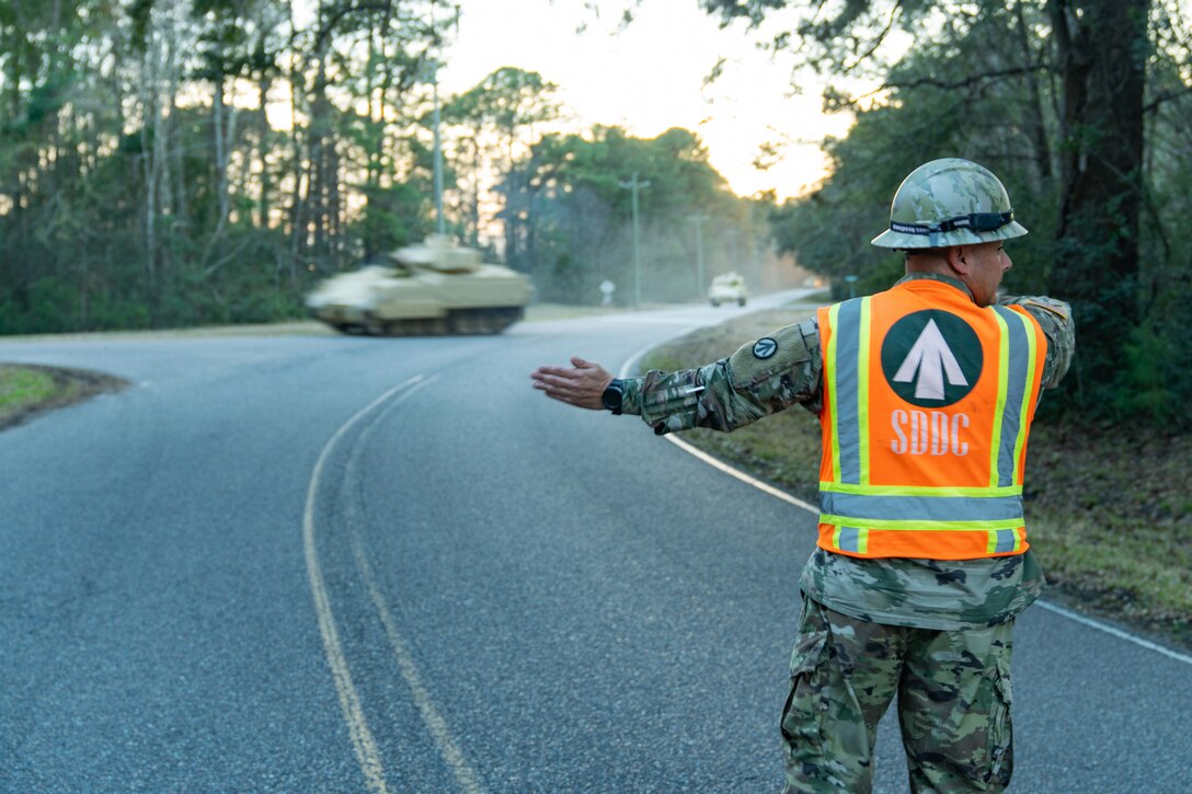 A soldier standing in the road directs Bradley vehicles to their destination.
