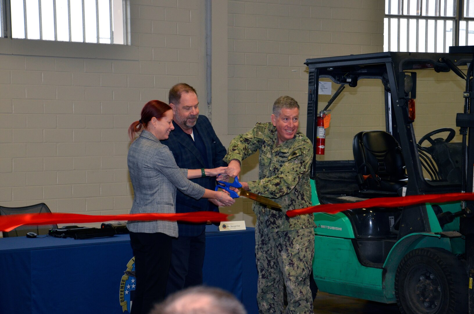 Three people cutting ribbon with ceremonial scissors.