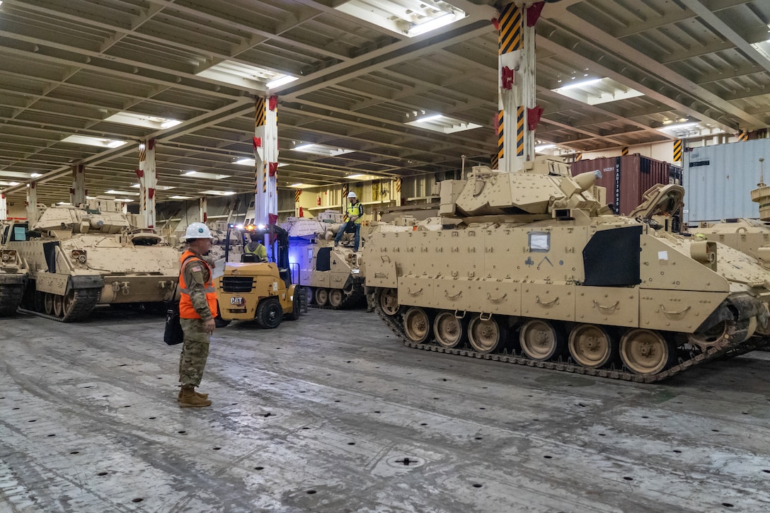 A soldier visually inspects rows of Bradley vehicles.