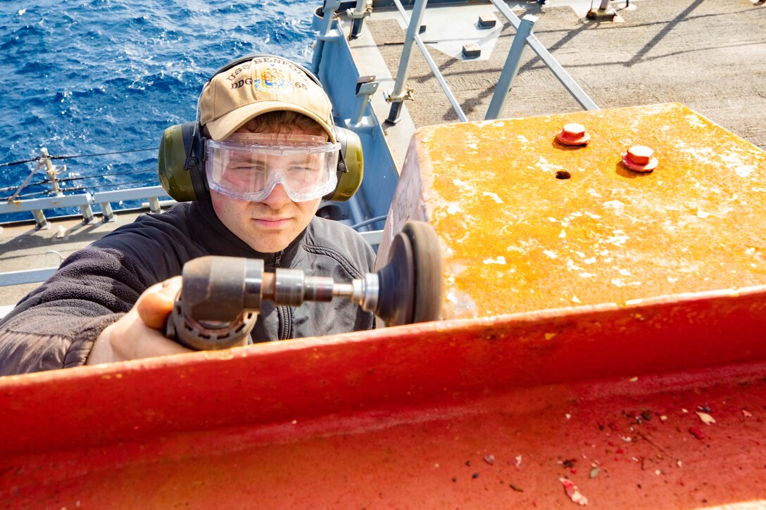 A sailor wearing goggles uses a buffing tool aboard a Navy ship.