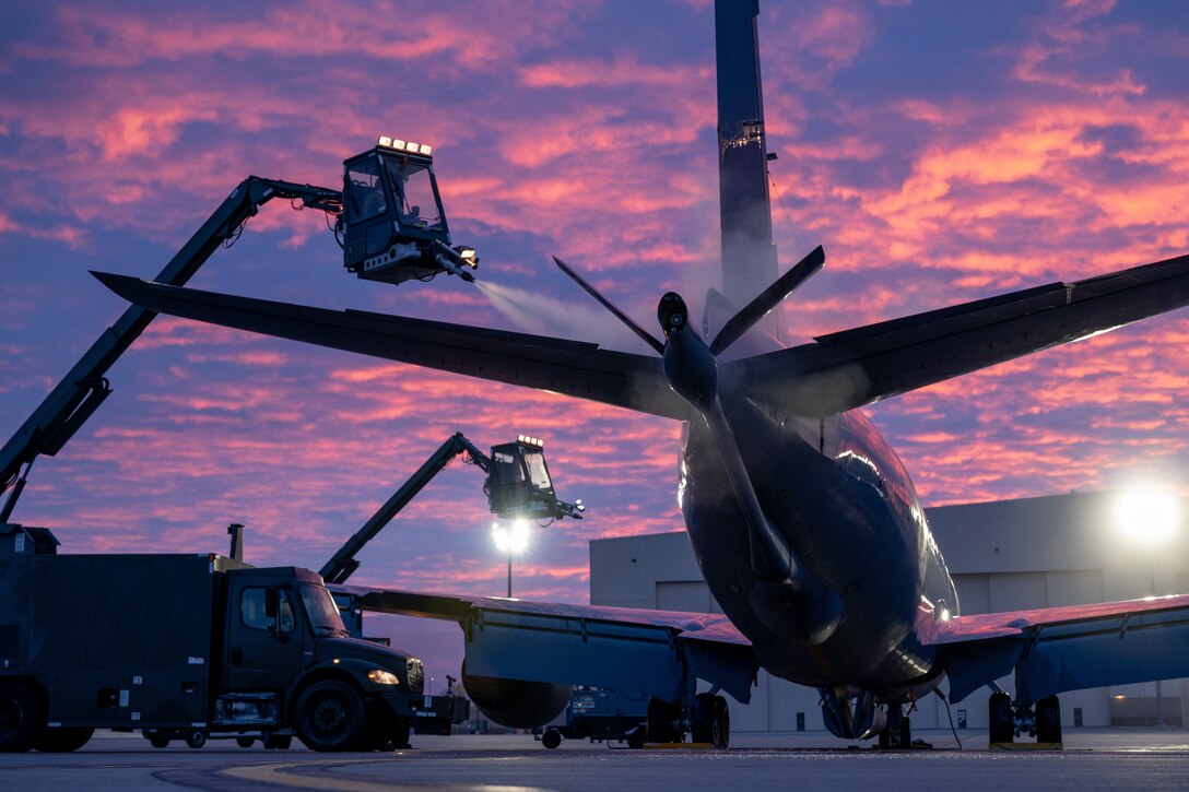 Airmen spray a de-icing agent onto a large plane from a bucket crane.