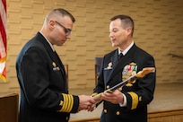Rear Adm. Dennis Collins, right, Commander, Navy Expeditionary Logistics Support Group, and Fourth Navy Expeditionary Logistics Regiment (NELR) Command Master Chief Stephen Jones, present challenge coins to 4th NELR Sailors during the decommissioning ceremony of 4th NELR at Naval Station Mayport, Florida, Jan. 20, 2023.