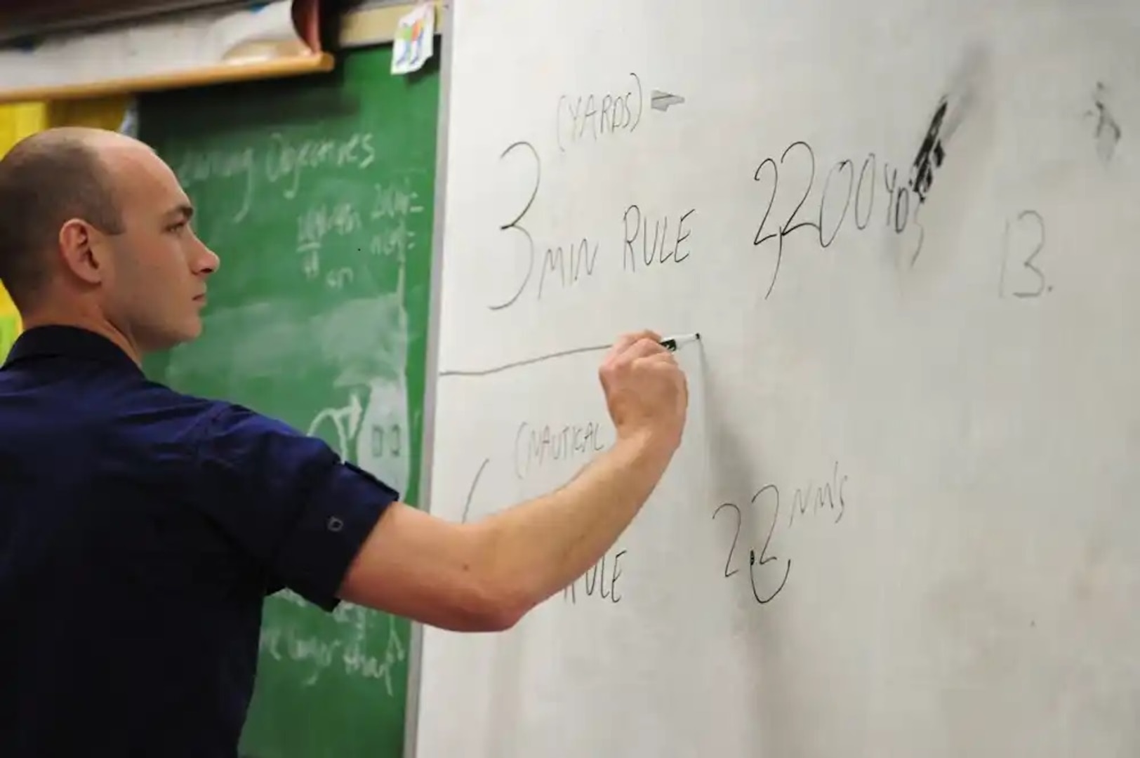 Petty Officer 2nd Class Brett Rielly, a boatswain's mate stationed at Coast Guard Station Juneau, Alaska, writes out an equation used to calculate distance in Jody Levernier's sixth-grade math class at Dzantik'i Heeni Middle School April 19, 2013. This event marked the fifth consecutive year that Levernier invited Coast Guard personnel to her class to show students how practical math is in the real world. U.S. Coast Guard photo by Petty Officer 3rd Class Grant DeVuyst.