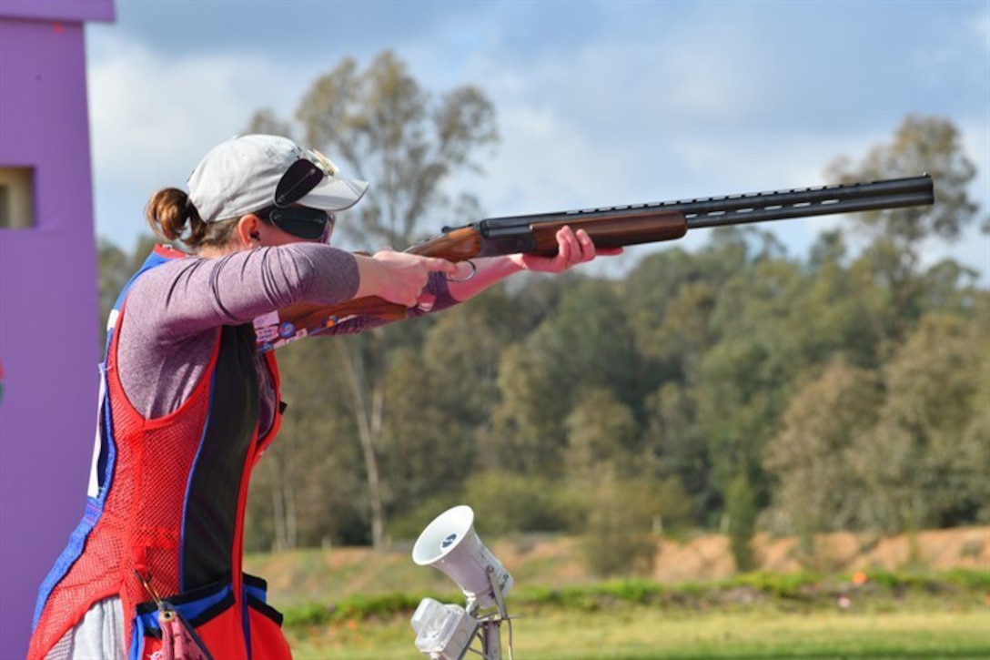 A soldier wearing shooting gear stands and aims a rifle.