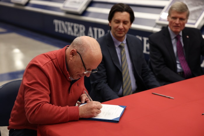 Man signing document at table watched by two others