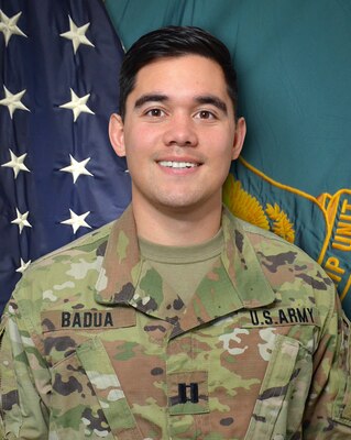 Male Soldier in uniform standing in front of two flags.