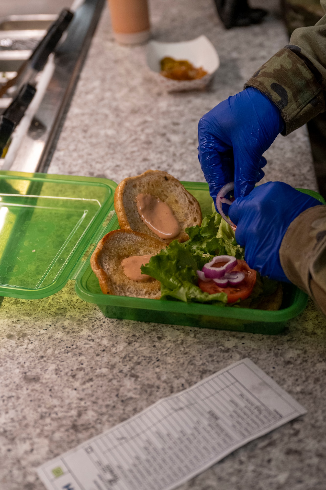 Airman 1st Class Hunter Pearson, 4th Force Support Squadron food service specialist, assembles a cheeseburger in an OZZI reusable food container at Seymour Johnson Air Force Base, North Carolina, Jan. 24, 2023. The OZZI food container is a replacement for previously used foam takeout containers to cut down on both costs and generated waste. (U.S. Air Force photo by Senior Airman Kevin Holloway)