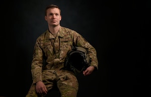 An Airman sits on a stool with his pilot helmet tucked under his arm.