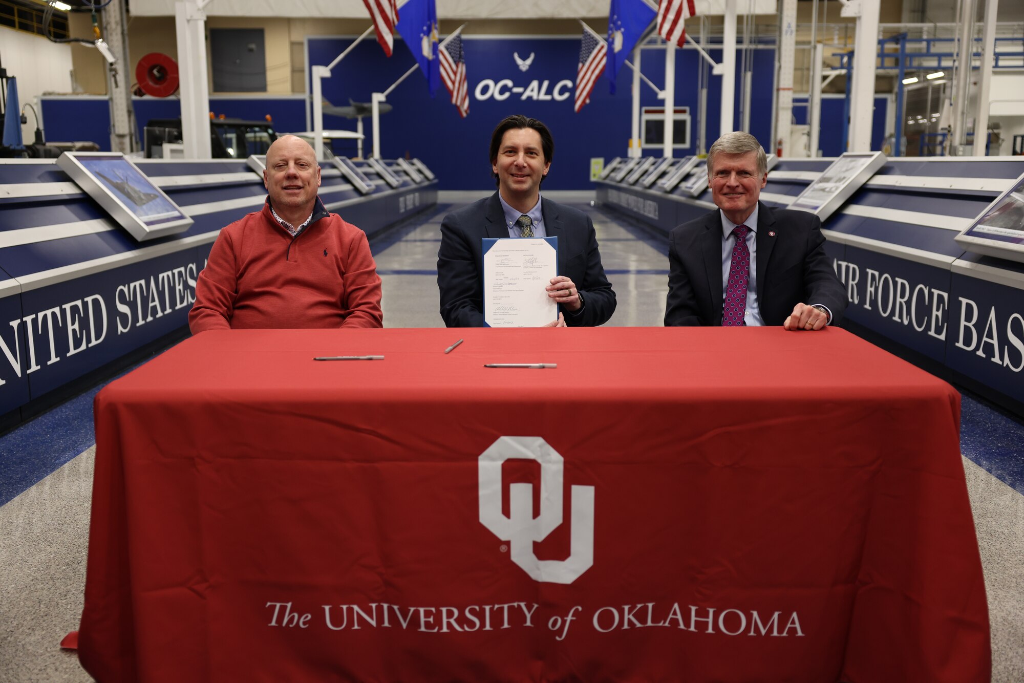 Three men at table posing for picture with document