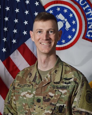 Male Army Soldier in uniform in front of U. S. Flag and USAREC flag.