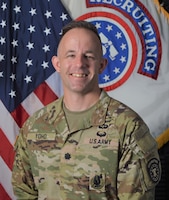 Male Soldier posed in front of the U.S. flag and the U.S. Army Recruiting Command flag.
