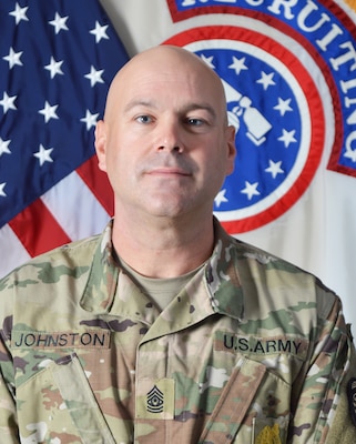 Male Soldier posed in front of the U.S. flag and the U.S. Army Recruiting Command flag.