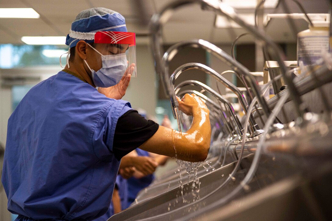 A soldier wearing personal protective equipment washes their arm in a sink.