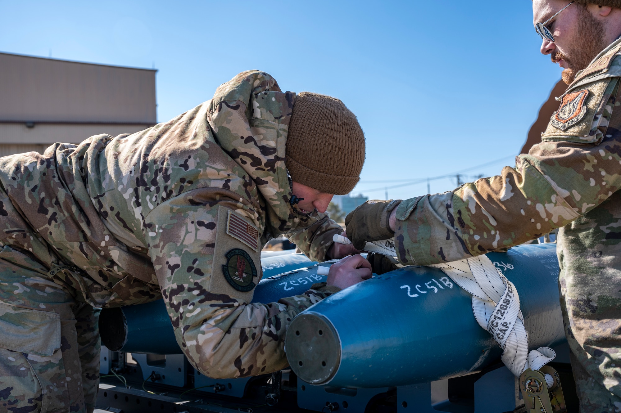 U.S. Air Force Tech. Sgt. Jacob Salwey, 51st Munitions Squadron (MUNS) maintenance pro super, and Staff Sgt. Joshua Sandy, 51st MUNS munitions inspector, write weapons stock numbers onto simulated GBU-38 Joint Direct Attack Munitions during a training event at Daegu Air Base, Republic of Korea, Jan. 30, 2023.