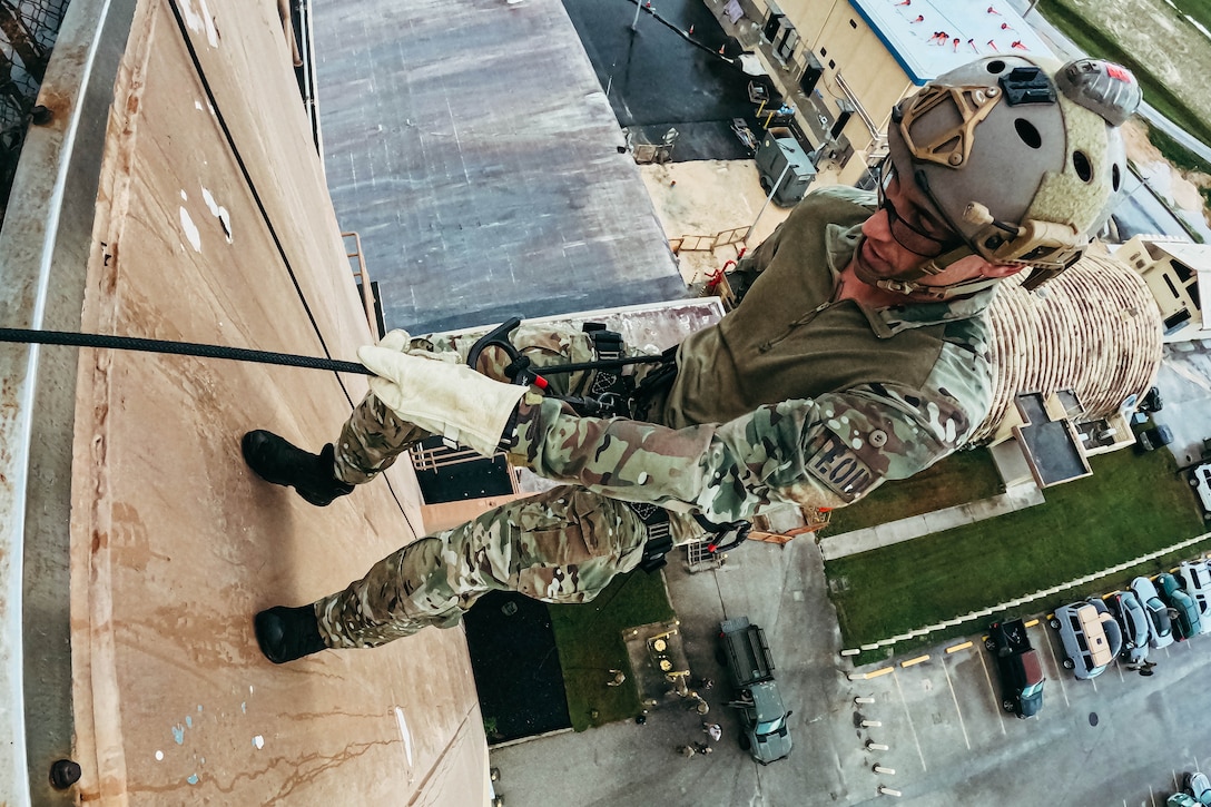 Close-up of a sailor rappelling down a tower in daylight.