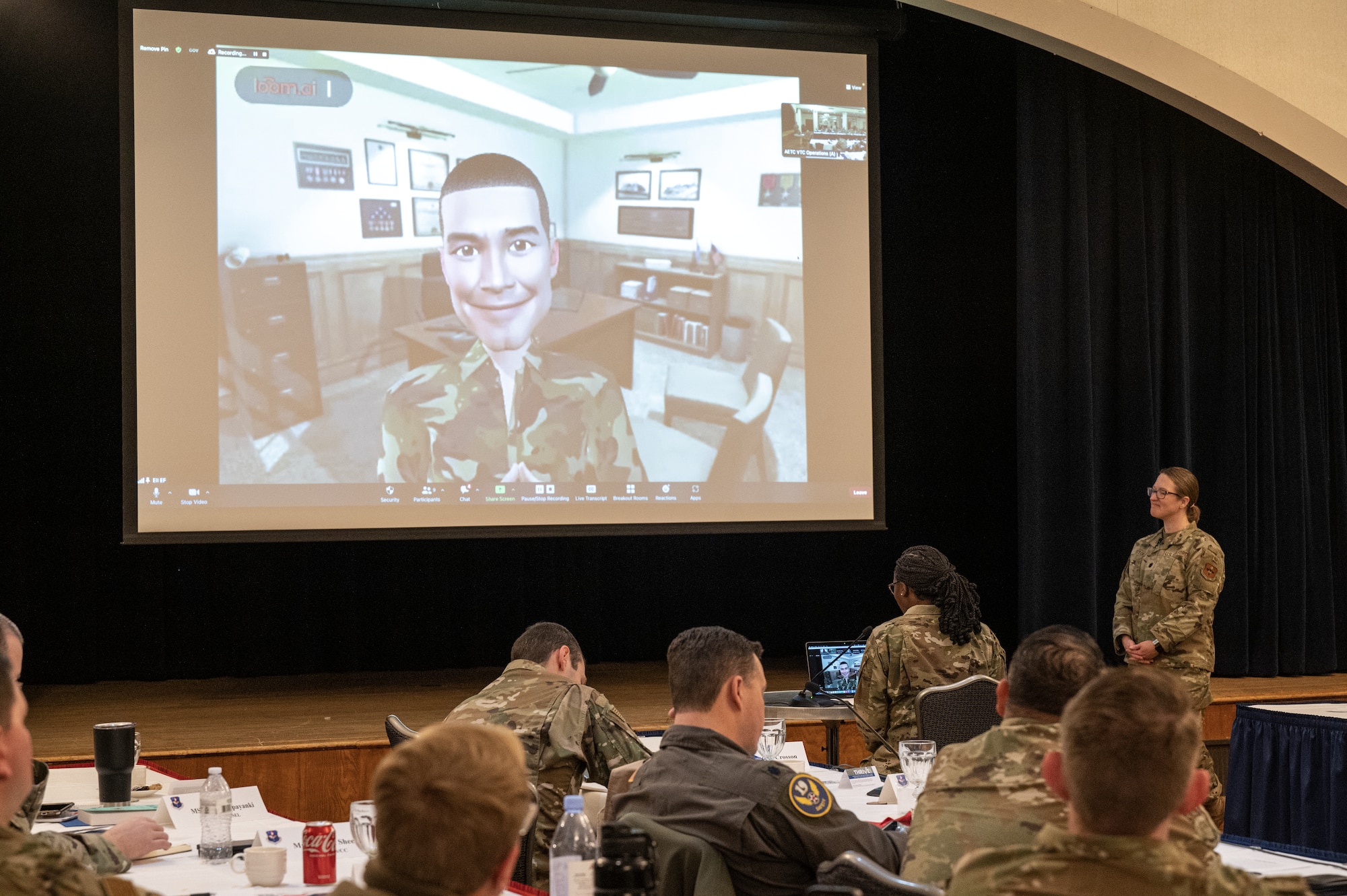 Airmen in large room with avator on pull down screen