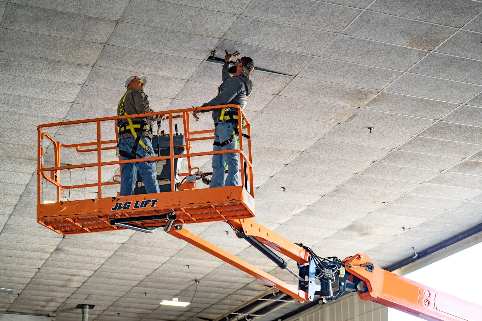 Two male workers on crane in aircraft hanger