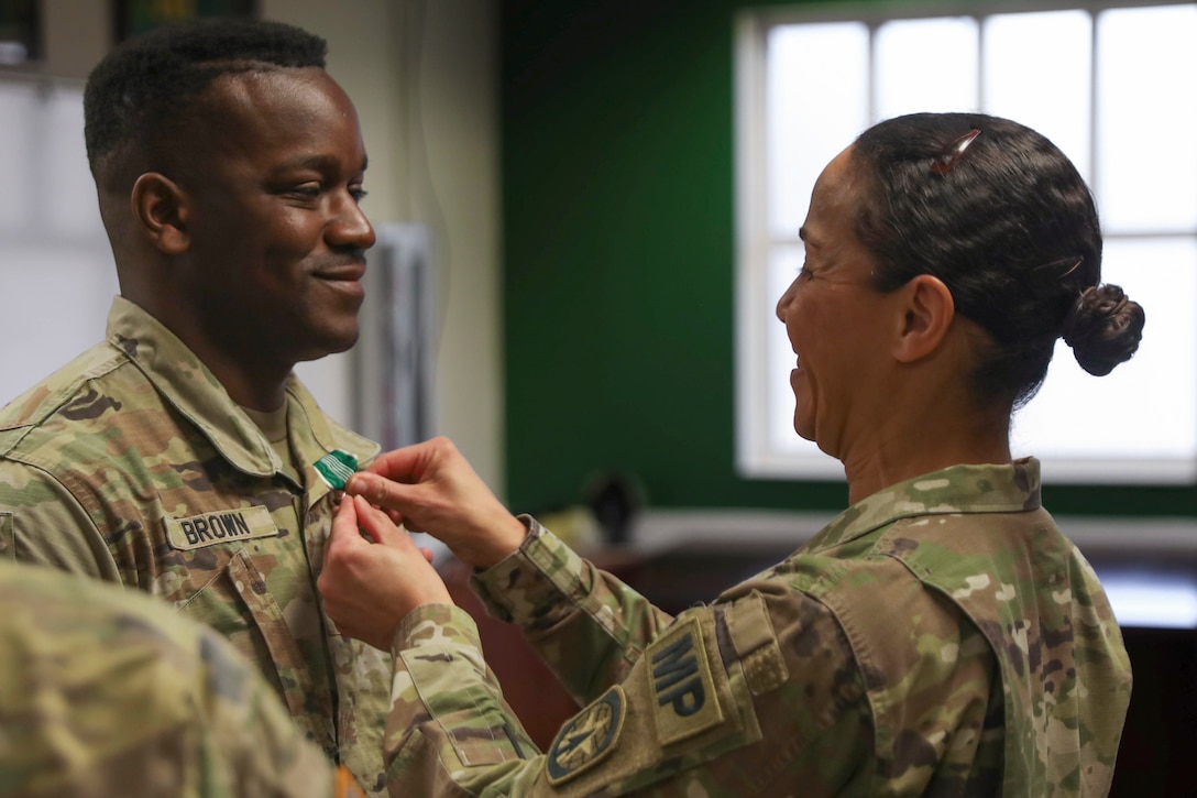 A soldier places a medal on another soldier’s collar.