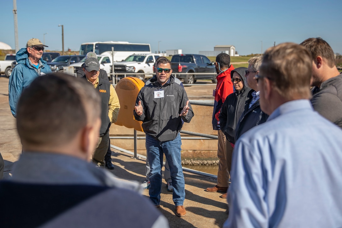 one person in military uniform speaks with several people in the background