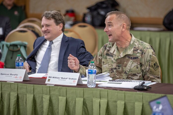 two people seated at table, one speaking