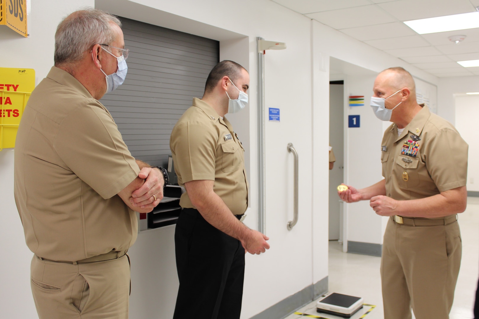 Three naval officers in khaki uniforms, with one holding a gold command coin.