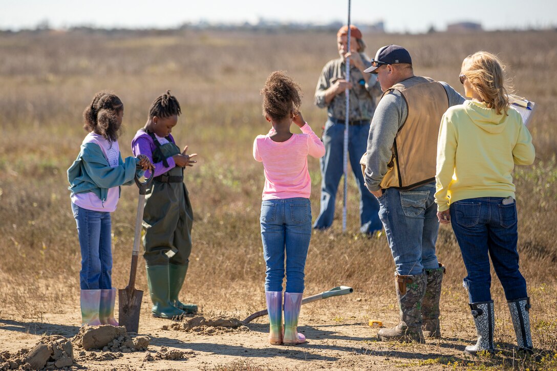 one child surveys a grassy area while other adults and children look on