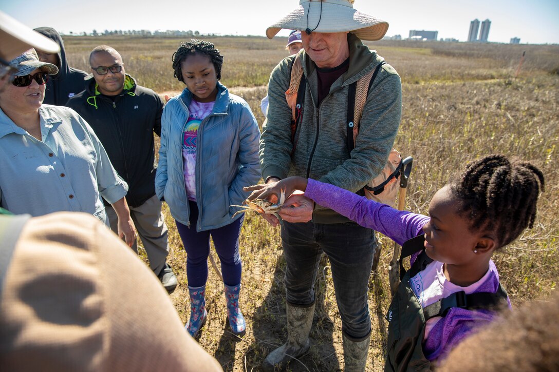 An adult holds a live blue crab while other adults and children look on