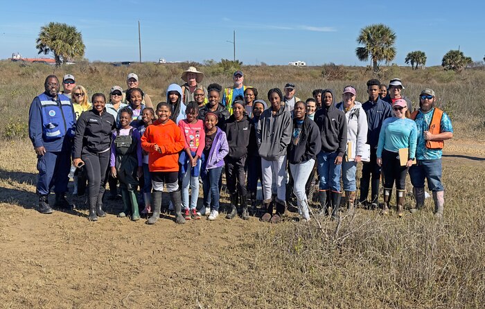 Adults and children pose for a group photo in tall grass with palm trees