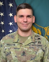 Man in U.S. Army uniform standing in front of two flags.