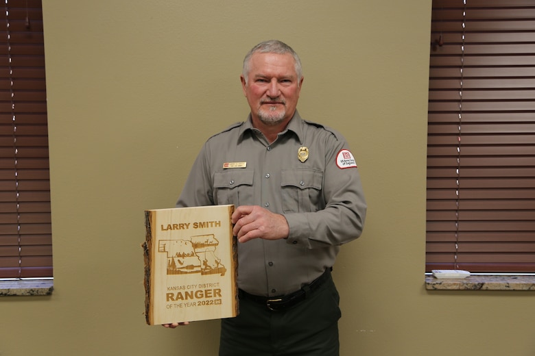Man in park ranger uniform stands with wooden award in his hands.