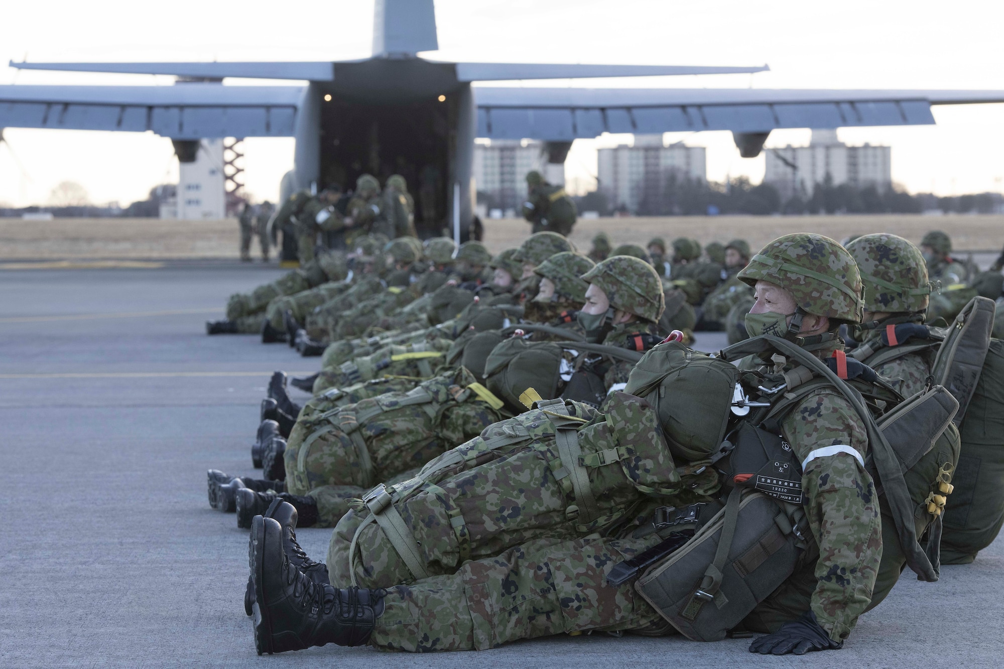 dozens of Japanese paratroopers lay on the flightline in front of a cargo plane