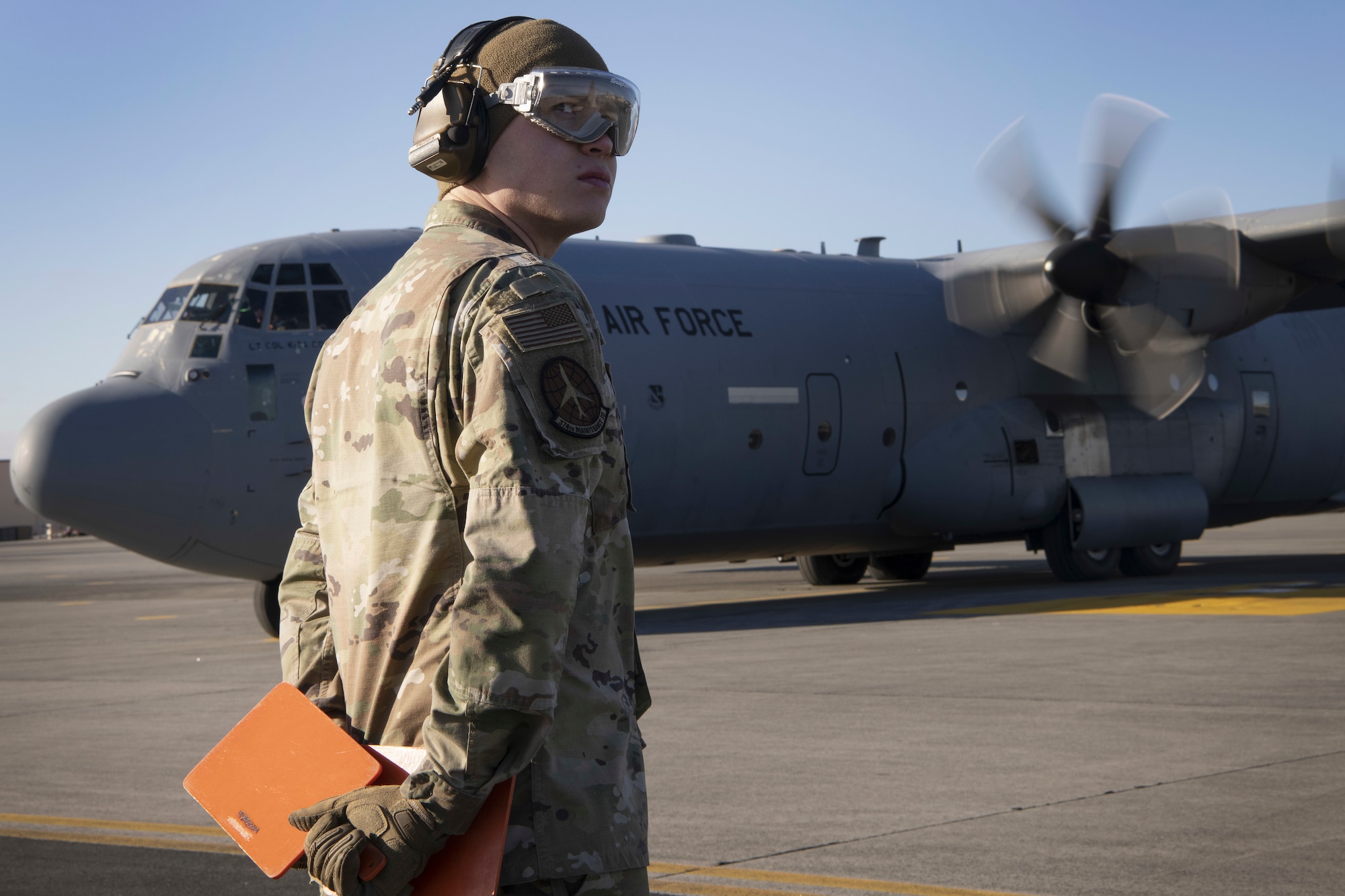 An airman holding signal cards stand on a runway in front of a cargo plane