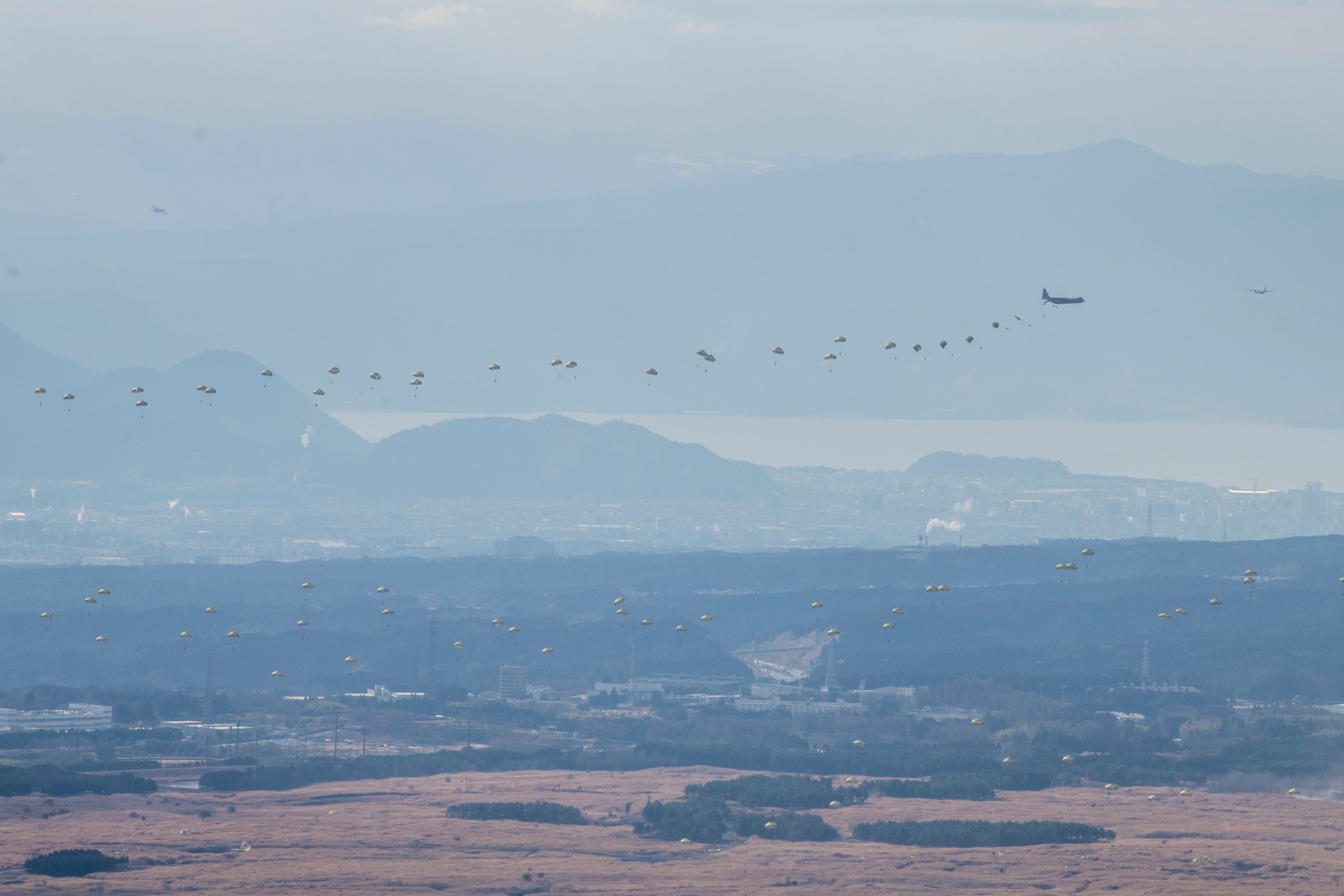 a plane drops paratroopers across an airfield