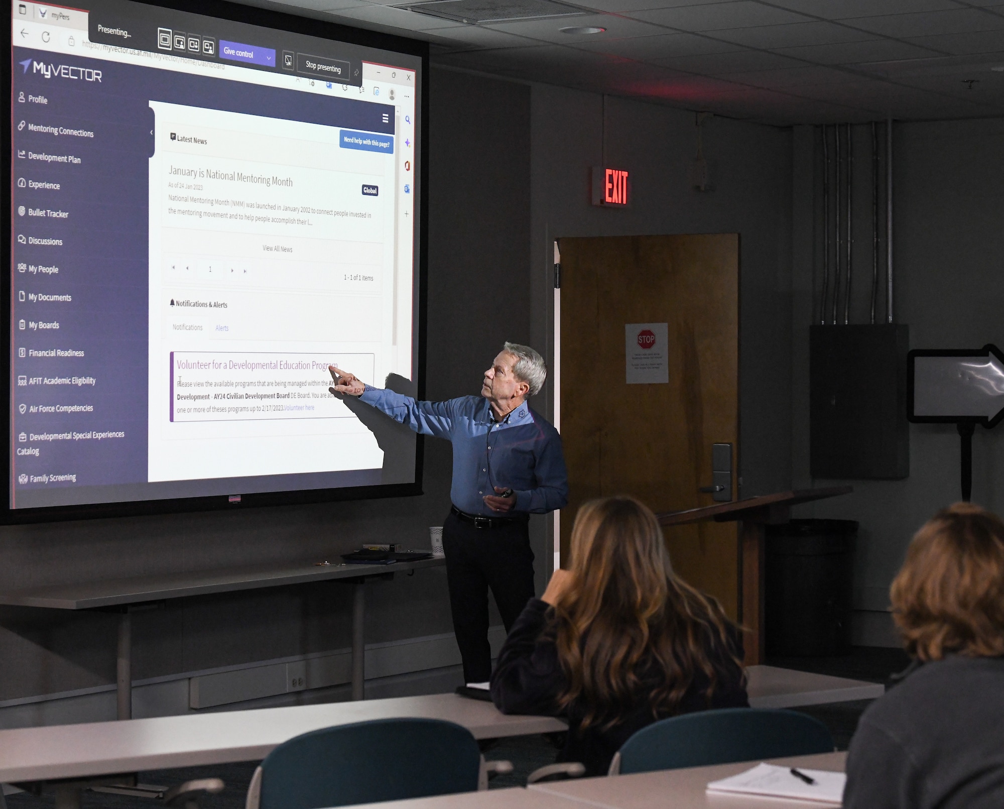 Mike Dent, Chief, Technical Management Branch, Plans and Programs Division, Arnold Engineering Development Complex, gives a presentation on Civilian Developmental Education. Dent is standing and pointing at a projector screen.