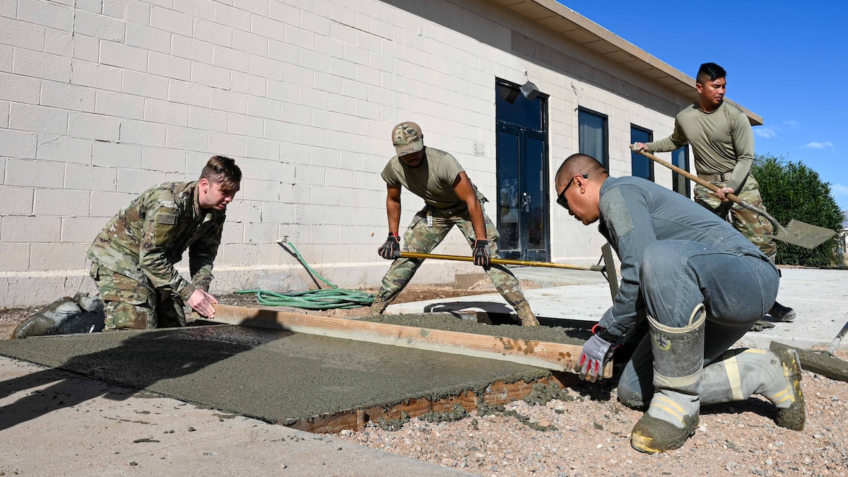 A photo of men in military uniforms leveling poured concrete
