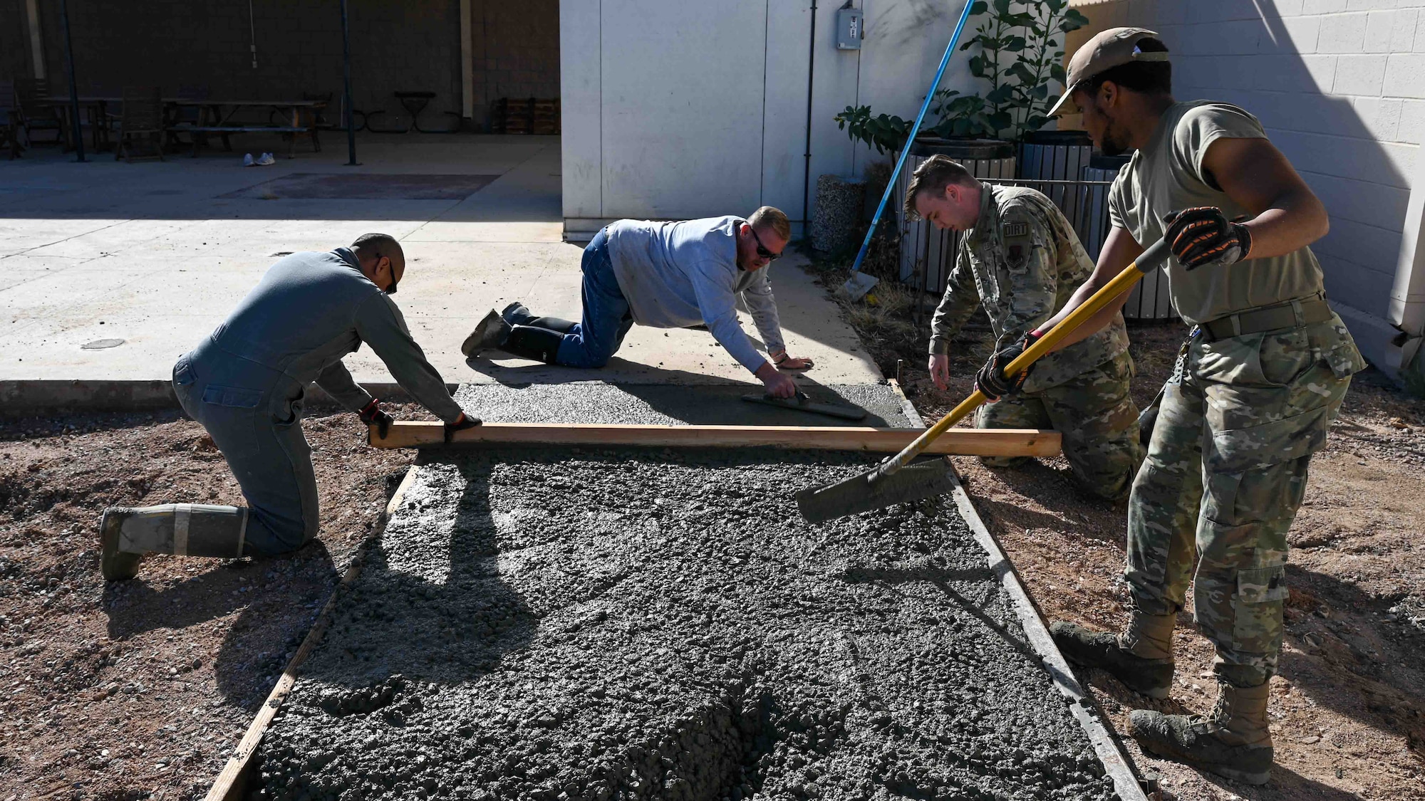 A photo of men in military uniforms leveling out poured concrete.