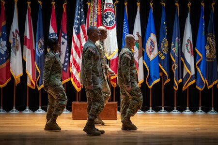 four people wearing u.s. army uniform pass a flag on a pole between them.