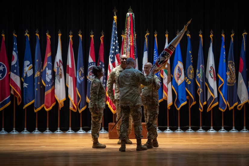 four people wearing u.s. army uniform pass a flag on a pole between them.