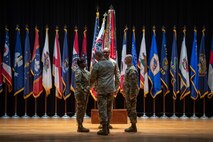 four people wearing u.s. army uniform pass a flag on a pole between them.