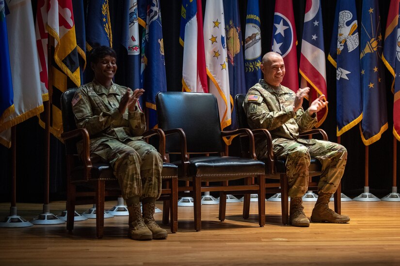 a man and a women wearing u.s. army uniform clap while seated in chairs.