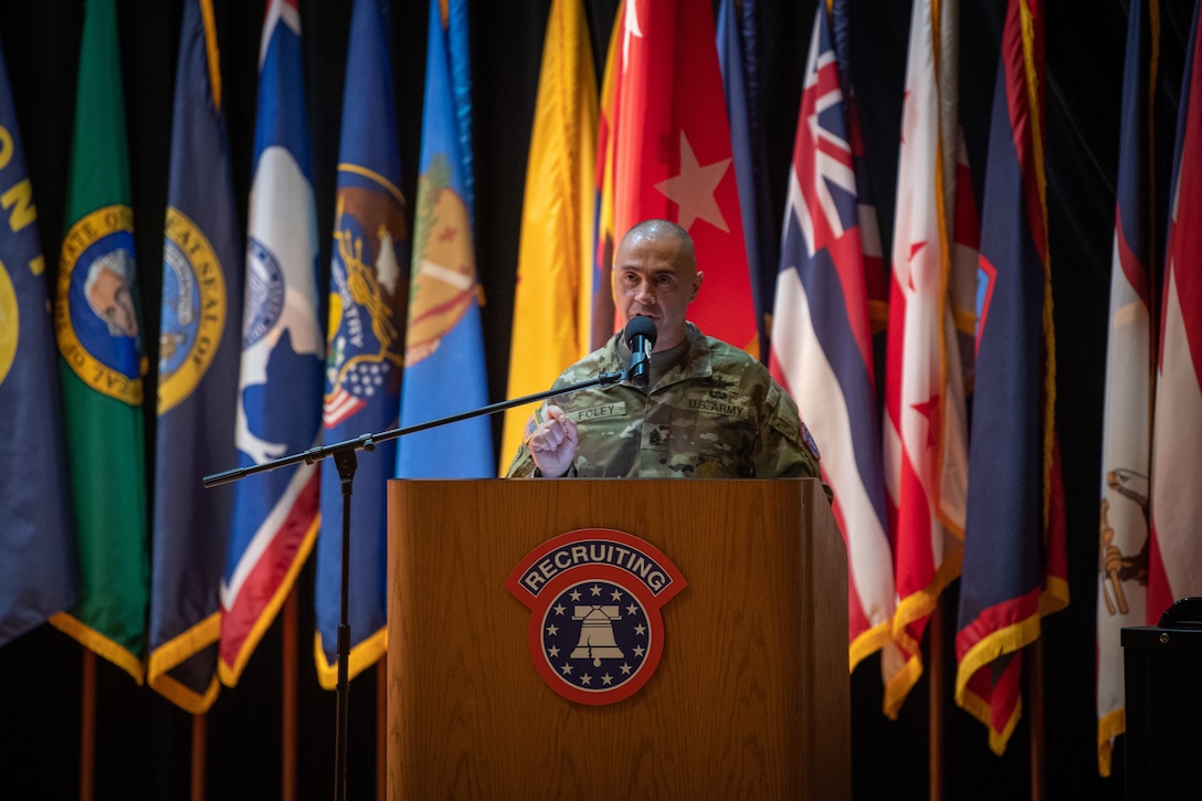 man standing in front of flags wearing u.s. army uniform.