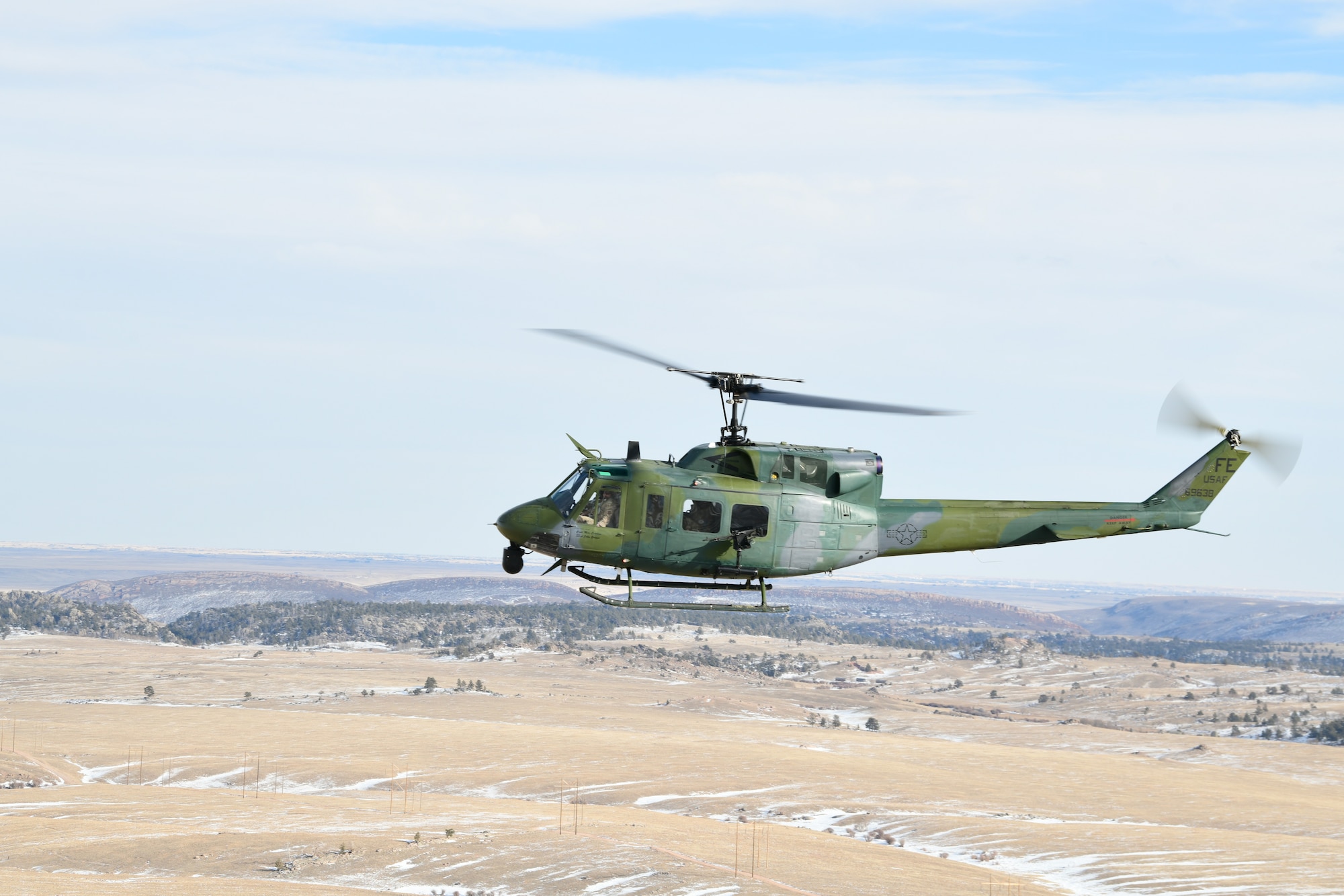 A helicopter from the 37th Helicopter Squadron flies over fields and hills in southeast Wyoming, February 15, 2022. The 37 HS flies through many different types of terrain for training purposes in order to stay mission ready and lethal at all times. (U.S. Air Force photo by Airman Sarah Post)