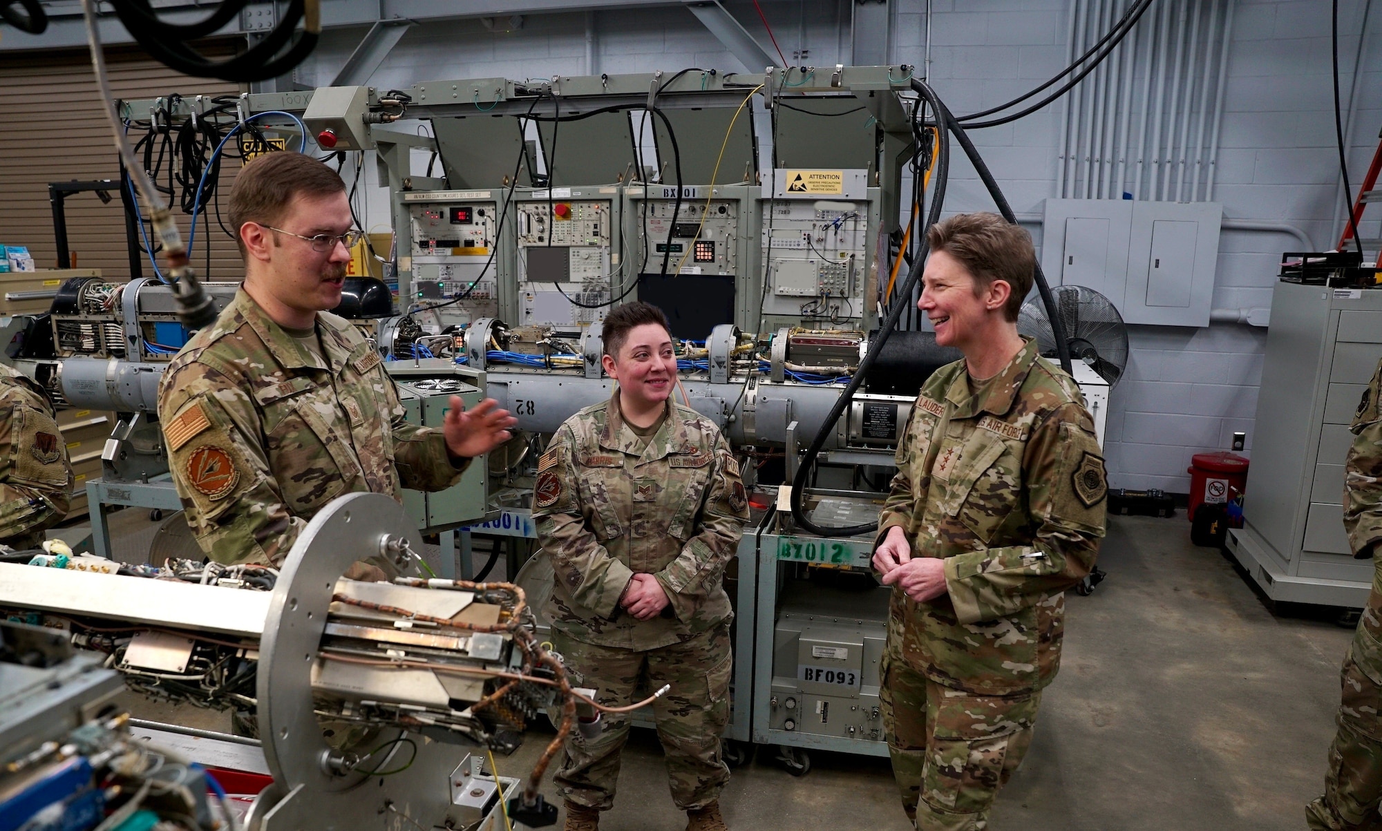 U.S. Air Force Tech. Sgt. Garrett Fox, 36th Electronic Warfare Squadron pod maintenance NCOIC, left, and Staff Sgt. Catherine Harris, 36th EWS electronic warfare systems craftsman, center, brief Lt. Gen. Leah G. Lauderback, deputy chief of staff for intelligence, surveillance, reconnaissance and cyber effects operations, right, on the Reclamation of Electronic Attack Pods (REAP) Program during her visit to the 350th Spectrum Warfare Wing at Eglin Air Base, Fla., Feb. 1, 2023. The REAP program aims to leverage resources from the 350th SWW and provide the receiving, diagnostic testing, recoupment, and shipment of EA pod equipment back into the supply chain for future use. (U.S. Air Force photo by 1st Lt. Benjamin Aronson)  (This photo has been altered for security purposes by blurring out computer monitors.)