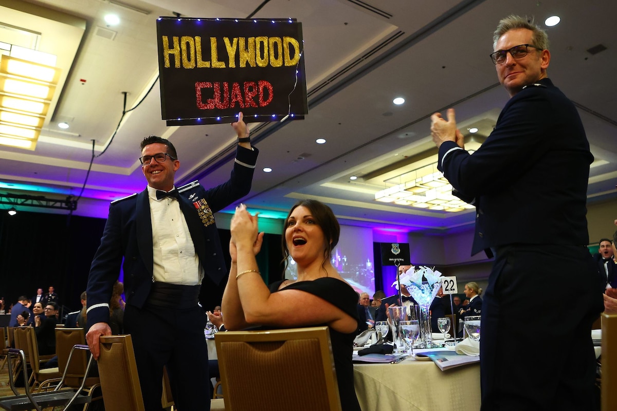 U.S. Air Force Col. Matt Glynn, left, vice wing commander of Cal Guard's 146th Airlift Commander, holds a Hollywood Guard sign as other members of his table cheer for one of the wing's award nominees, Jan. 21, 2023, in Anaheim, California, during the California National Guard’s Service Member of the Year banquet. The event honored members of the California Army National Guard, California Air National Guard and California State Guard for outstanding duty performance in 2022. (U.S. Air National Guard photo by Staff Sgt. Crystal Housman)