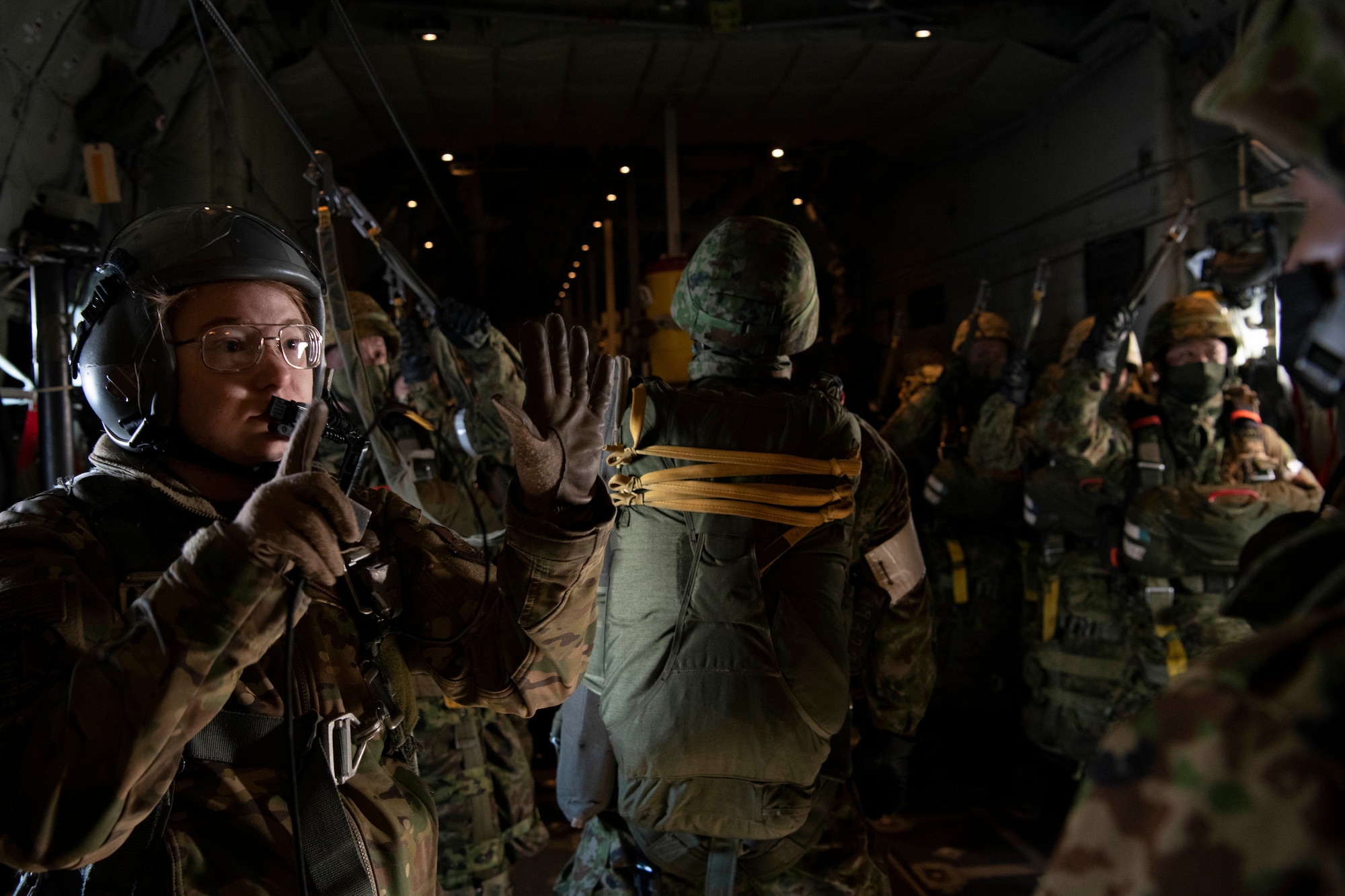 one soldier signals to a dozen others inside a plane cargo bay