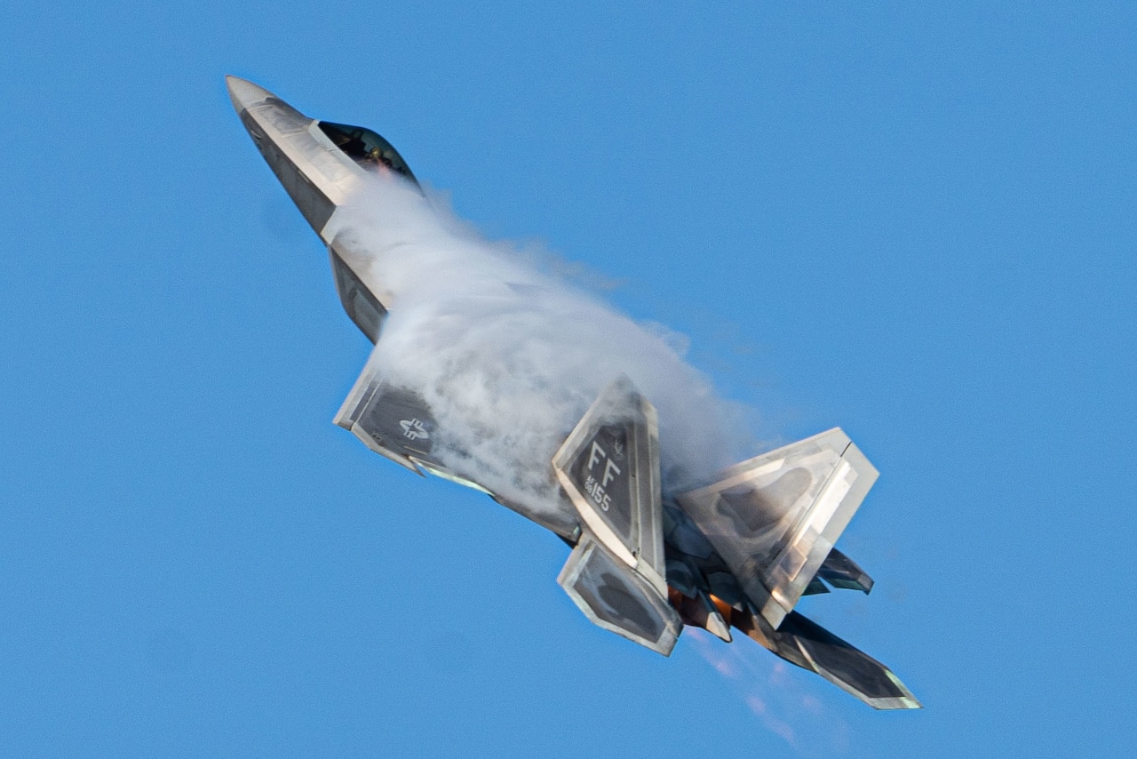 An F-22 flies across a blue sky.