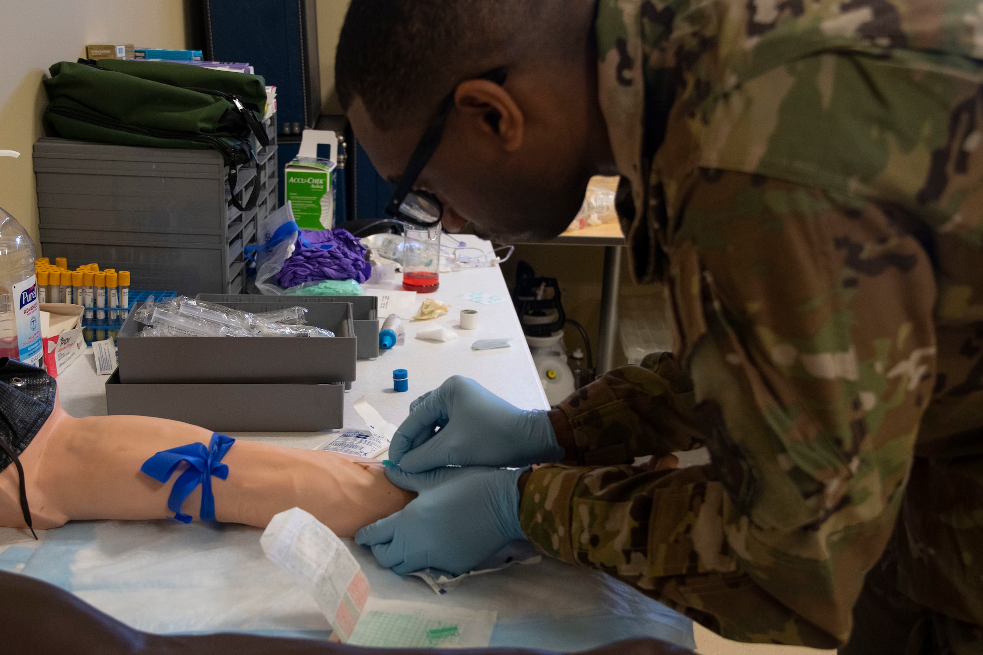 An Airman sticks a catheter into a prosthetic arm as a part of training.