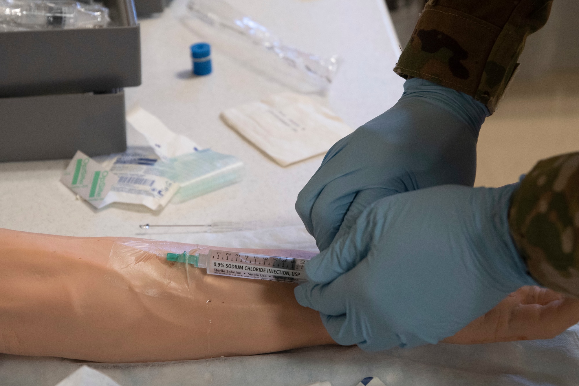 An airman sticks a needle into a prosthetic arm as a part of training.
