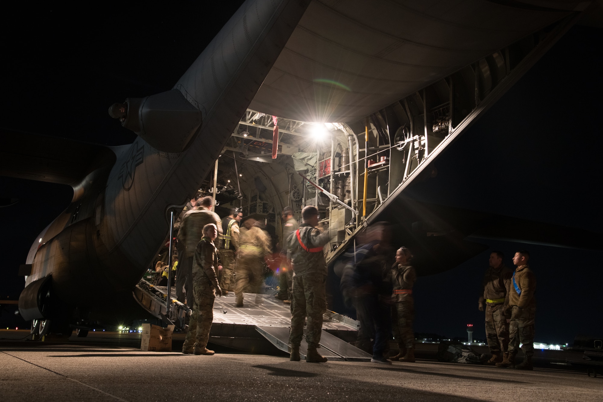 Blurry Airmen move in and out of the cargo bay of an in-focus parked C-130 at night transporting patients and medical equipment.