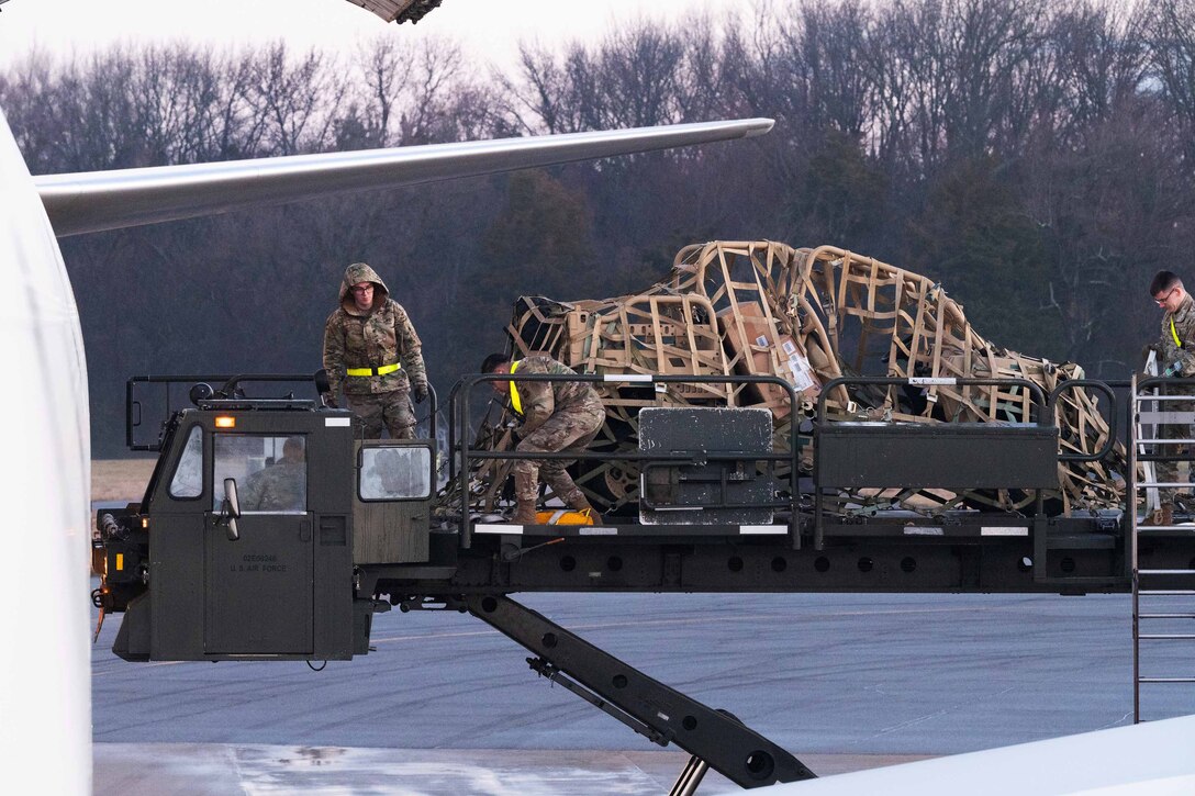 Airmen stand on a lift and load equipment into an aircraft.